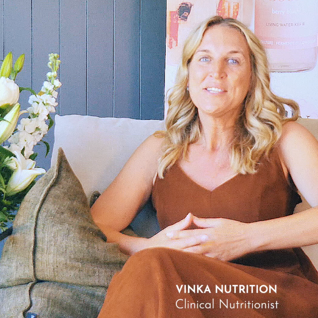 Woman in a brown dress sitting on a couch with flowers and a blue wall in the background, branded 'Vinka Nutrition'.